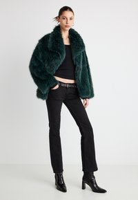 Chaqueta de piel sintética en verde oscuro, top ajustado negro, vaqueros acampanados negros y botines negros. La chaqueta presenta un cuello ancho y un acabado texturizado.