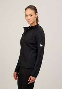 Giacca sportiva nera con zip frontale, cappuccio e polsini con foro per il pollice, realizzata in tessuto texturizzato con un accento del logo sulla manica.