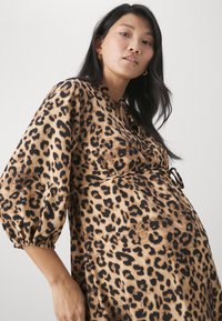 Robe imprimée léopard en beige et noir, avec des manches ballon, une taille cintrée avec un lien, et un tissu lisse et texturé.