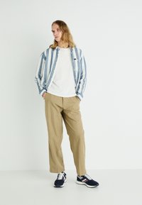 Light blue and white striped button-up shirt, white t-shirt, beige wide-leg trousers, and navy sneakers with accents. Simple, casual design.