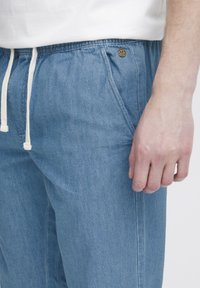 Pantalones de mezclilla azul claro con cordón, que presentan una cintura elástica, bolsillos laterales y un pequeño detalle de logo metálico.