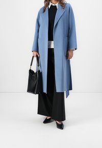 Jasnoniebieski wełniany płaszcz z klapami, dwie przednie kieszenie, w połączeniu z czarną bluzką, czarnymi szerokimi spodniami i czarnymi balerinami w szpic.