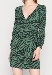Robe portefeuille à manches longues avec imprimé zèbre vert et noir, décolleté en V et détail noué à la taille. Confectionnée en tissu doux et léger.