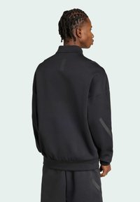 Sudadera de forro polar negra con cuello alto, corte relajado y sutiles detalles reflectantes en las mangas. Textura suave, sin patrones.