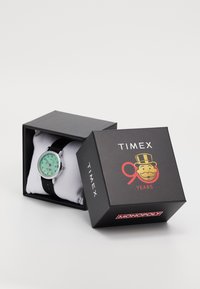 Orologio Timex con quadrante verde menta, cassa argentata e cinturino in pelle nera, presentato in una scatola nera con il marchio del 90° anniversario di Monopoly.