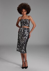 Musta ja hopea paljeteista valmistettu kahden osan asu, jossa on olkaimeton crop-top ja puolipitkä hame, tiukalla siluetilla ja kimaltelevalla efektillä.