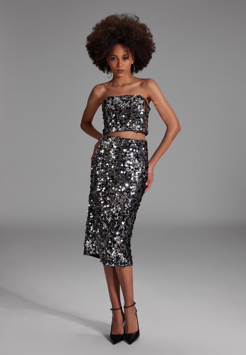 Musta ja hopea paljeteista valmistettu kahden osan asu, jossa on olkaimeton crop-top ja puolipitkä hame, tiukalla siluetilla ja kimaltelevalla efektillä.