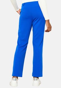 Blå byxor med raka ben i ett slätt tyg. Har hög midja, diskreta bakfickor och kombineras med vita sneakers.