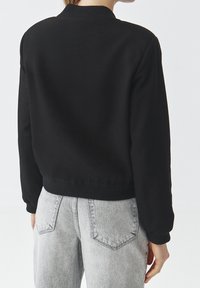 Černá mikina s ribbovaným výstřihem a manžetami, zkrácená délka, spárovaná se světle šedými džíny s vysokým pasem, zadními kapsami a vybledlou texturou.