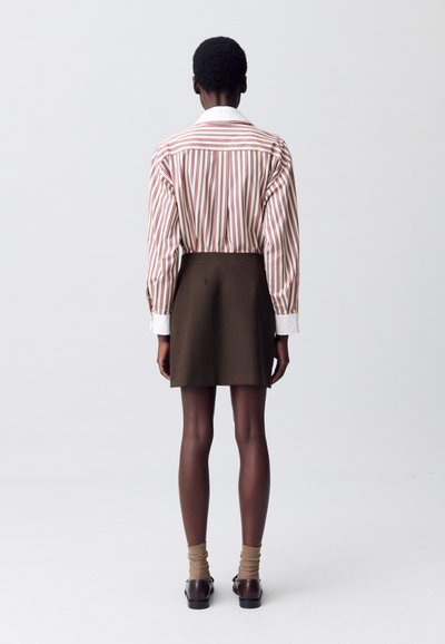 Camicia a righe bianca, rossa e marrone, abbinata a una gonna marrone. Presenta maniche lunghe e colletto classico, con un design aderente.