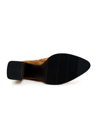 Béžová nubuková vysoká bota na podpatku s špičatou špičkou, texturovanou černou gumovou podrážkou a vrstveným podpatkem. Jednoduchý design bez ozdob.