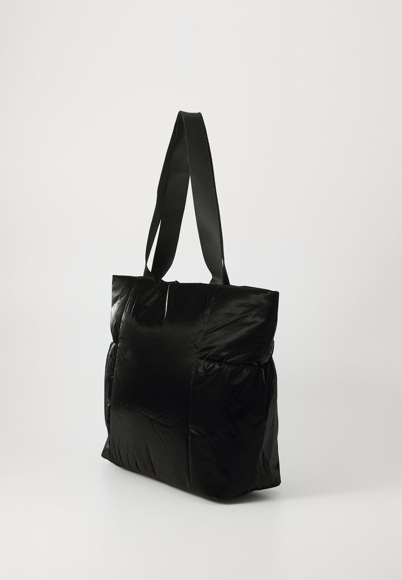 Bolsa tote negra, acolchada, con una superficie texturizada y dos asas amplias de tela. Forma rectangular, acabado brillante, material suave y flexible.