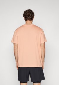Camiseta de manga corta en color durazno con escote redondo y corte relajado, combinada con pantalones cortos oscuros. Material de algodón, textura suave, sin patrones visibles.