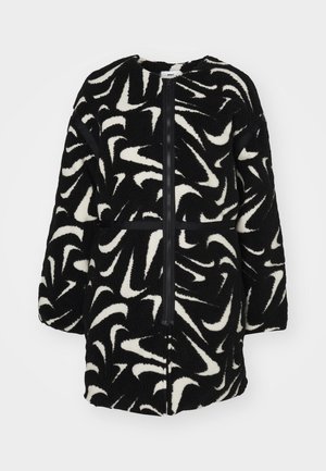 Svart og hvit fleecejakke med en virvlande mønster, glidelås foran og kontrasterende svarte detaljer på ermer og hofte.