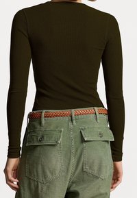 Top de manga larga verde oliva con textura acanalada combinado con pantalones cargo verde claro. Cinturón trenzado marrón con acentos metálicos.