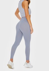 Szary crop top i legginsy wykonane z elastycznego materiału, charakteryzujące się eleganckim designem i subtelnymi detalami szwów, zestawione z białymi butami sportowymi.