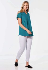 Tee in Türkis mit V-Ausschnitt und kurzen Ärmeln, kombiniert mit weißen Slim-Fit-Hosen und schwarzen Slippern. Glattes, leichtes Material; lässiges Design.