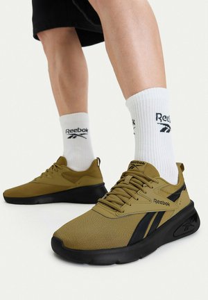 Person wearing olive green and black Reebok sneakers with white Reebok logo socks, standing on a white surface.