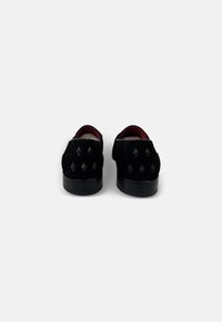 Zwarte suède schoenen met een platte zool, voorzien van een diamanten patroon op de achterkant en een contrasterende rode voering aan de binnenkant.