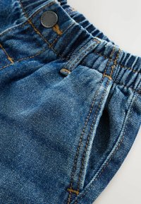 Pantalones cortos de mezclilla con cintura elástica, color azul, costuras visibles en un tono dorado en contraste y detalle de bolsillo lateral.
