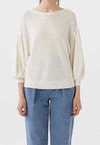 Suéter a rayas crema con mangas anchas y abullonadas y dobladillo acanalado. Combinado con pantalones de mezclilla azul de tiro alto y sueltos.