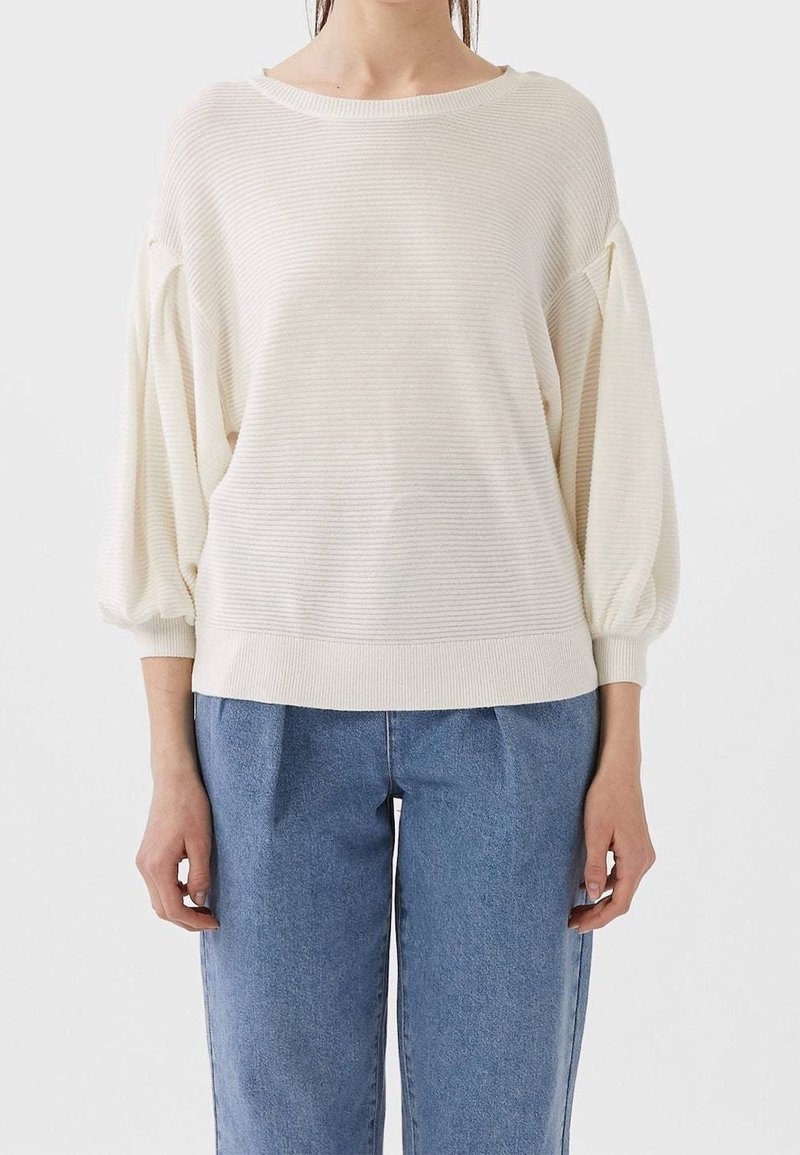 Suéter a rayas crema con mangas anchas y abullonadas y dobladillo acanalado. Combinado con pantalones de mezclilla azul de tiro alto y sueltos.