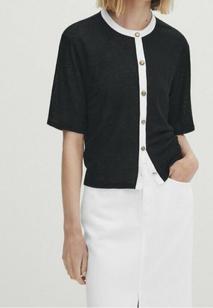 Black short-sleeve cardigan made of lightweight material, featuring a white collar and button placket, paired with a white skirt.