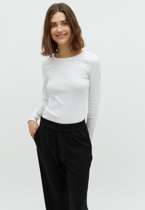 White long-sleeve top with a rounded neckline and ribbed texture paired with loose-fitting black trousers featuring an elastic waistband.