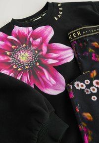 Sudadera negra con un gran gráfico de flor rosa en el frontal, con acentos en verde y blanco. Etiqueta de la marca "BAKER" en dorado en el cuello.