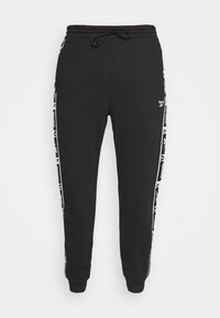 Svarta träningsbyxor i mjukt tyg, med dragsko i midjan och vita sidostråk med logodetalj. Öppning med mudd vid vristen.