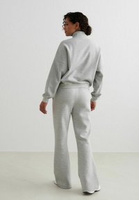 Gray cotton tracksuit featuring a high collar, loose fit, and flared pants. Smooth texture with ribbed cuffs and waistband.