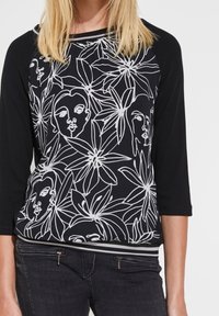Czarnobiały top z kwiatowym wzorem i liniowym rysunkiem twarzy, z rękawami 3/4 i kontrastowym paskiem u dołu.