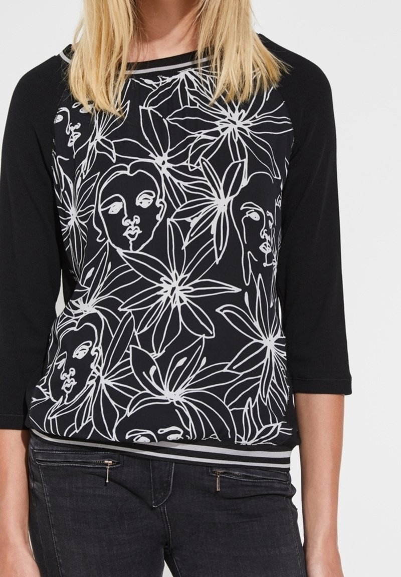 Czarnobiały top z kwiatowym wzorem i liniowym rysunkiem twarzy, z rękawami 3/4 i kontrastowym paskiem u dołu.