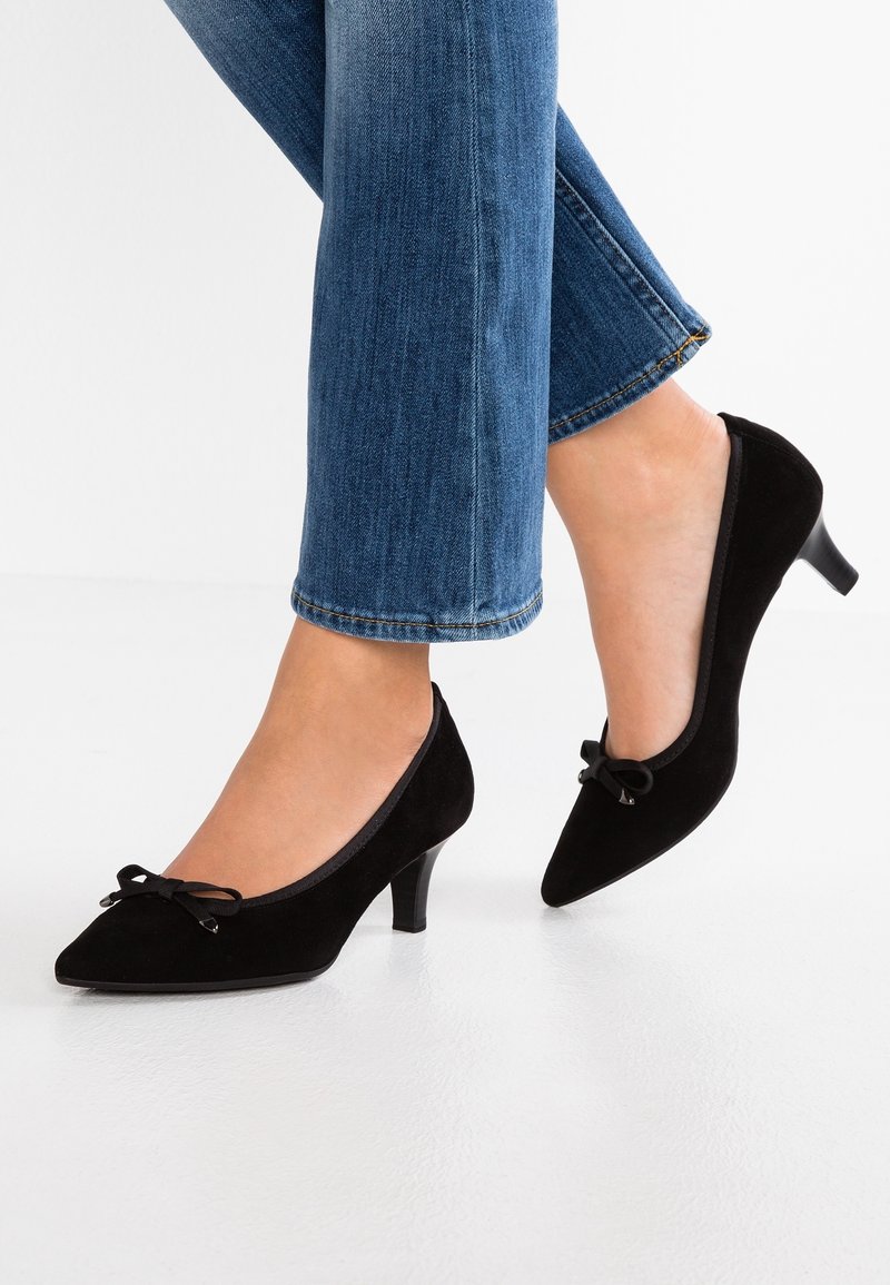 Escarpins en daim noir avec bout pointu, petit talon et détail nœud sur le dessus, associés à un jean bleu. Surface lisse et design classique.