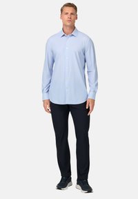 Camicia a maniche lunghe azzurro chiaro con un motivo a righe, colletto button-down e bottoni bianchi, abbinata a pantaloni scuri e scarpe sportive.