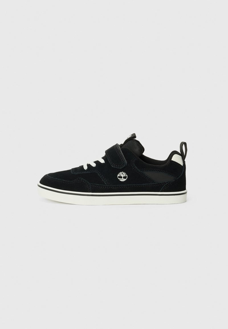 Sneaker en daim noir avec une semelle en caoutchouc blanc, dotée d'une sangle en Velcro et de lacets traditionnels. Logo affiché sur le côté.