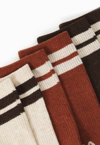 Chaussettes rayées dans des tons de rouille, crème et marron. Fabriquées en tissu tricoté, avec des poignets côtelés et des rayures horizontales.