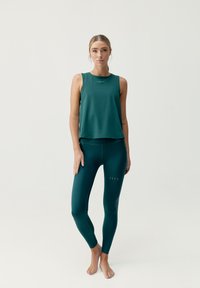 Top verde senza maniche abbinato a leggings high-waisted coordinati; entrambi presentano un design minimal con tagli sottili e una texture liscia.