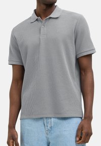 Grå kortærmet polo-shirt med struktureret stof og ribbet krave, der har en frontknapplacket og et lille logo på brystet.