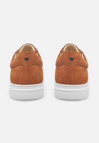 Scarpe in suede marrone con suola in gomma bianca, caratterizzate da una forma arrotondata e dettaglio intagliato sui talloni. Accento del logo nero sul retro.