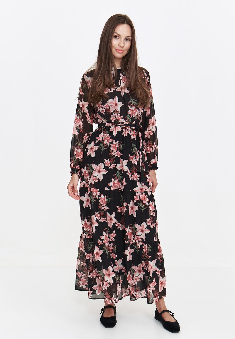 Floral maxi dress featuring a black sheer fabric with pink and green flower patterns, long sleeves, a belted waist, and tiered hemline.