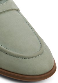 Close-up af lysegrøn ruskindssko med detaljeret syning og brun gummisålekant.