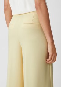 Gelbe weit geschnittene Hosen mit einer glatten Textur, ausgestattet mit zwei Gesäßtaschen und einem taillierten Bunddesign.