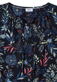Blusa a motivo floreale scuro con foglie e fiori blu, rosa e giallo pallido, caratterizzata da uno scollo rotondo con lacci e un'etichetta "CECIL" all'interno.