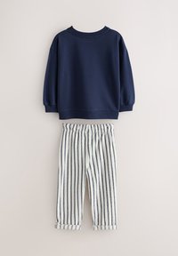 Bluză sport de culoare bleumarin cu guler tip rețea și mâneci lungi cu manșete, asortată cu pantaloni crem și bleumarin cu dungi, prevăzuți cu talie elastică.