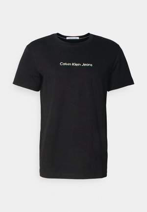 Schwarzes T-Shirt mit kurzen Ärmeln und Rundhalsausschnitt, mit dem weißen Text "Calvin Klein Jeans" zentriert auf der Brust.