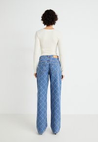 Light blue wide-leg jeans with a diamond pattern, featuring a high waist, five pockets, and a tan leather patch on the back.