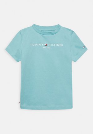 Jasnoniebieska koszulka dla małego dziecka z napisem "Tommy Hilfiger est. 1985" i logo na przodzie oraz napami na lewym ramieniu.