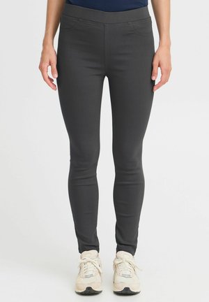 Temno sive legice z gladko teksturo, visoko pasom in slim fit krojem, z diskretno sprednjo šivom, v kombinaciji s svetlimi teniskami.