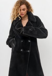 Schwarzer doppelt-knöpfiger Mantel mit großem Kragen, aus weichem Material. Verfügt über glänzende Knöpfe und taillierte Ärmel mit Manschettendetail.